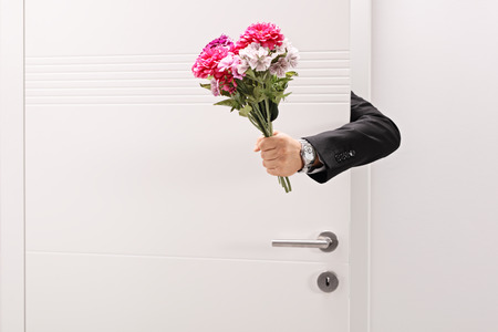 Person giving a flower bouquet from behind a doorの写真素材