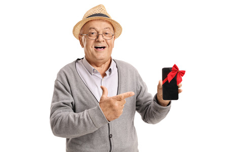 Mature man showing a phone wrapped with red ribbon as a gift and pointing isolated on white backgroundの写真素材