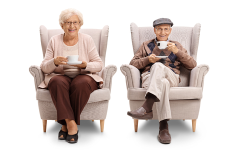 Seniors seated in armchairs drinking tea and looking at the camera isolated on white backgroundの写真素材