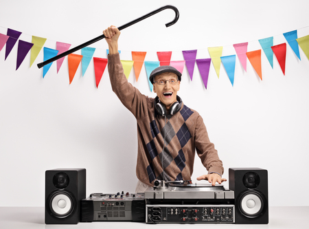 Overjoyed senior with a cane playing music on a turntable against a wall with decoration flagsの写真素材