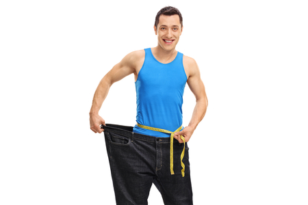 Young guy in oversized jeans measuring his waist isolated on white backgroundの写真素材
