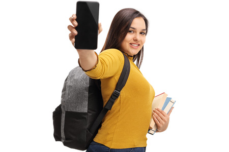 Female teenage student with a backpack and books showing a phone isolated on white backgroundの写真素材