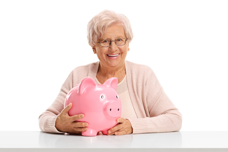 Senior lady with a piggybank seated at a table isolated on white backgroundの写真素材