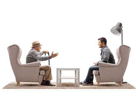 Elderly man and a young guy sitting in armchairs and having a conversation isolated on white backgroundの写真素材
