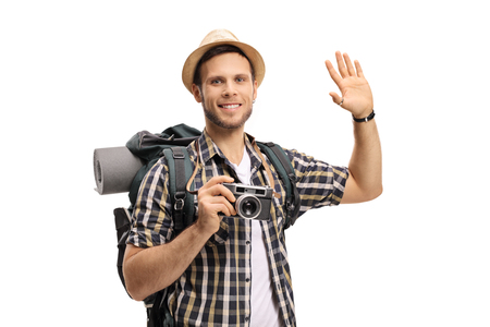Tourist with a camera and a backpack waving isolated on white backgroundの写真素材