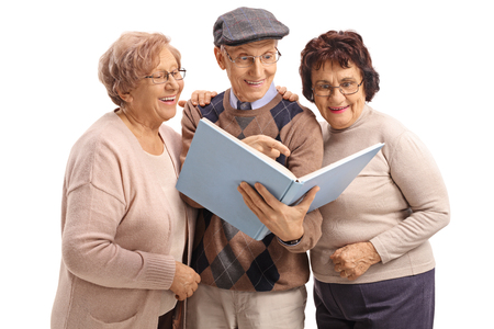 Two elderly women and an elderly man reading a book together isolated on white backgroundの写真素材