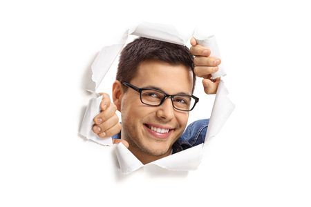 Young guy peeping through a paper hole and smiling isolated on white backgroundの写真素材