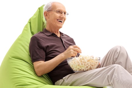 Senior seated on a green beanbag eating popcorn isolated on white backgroundの写真素材