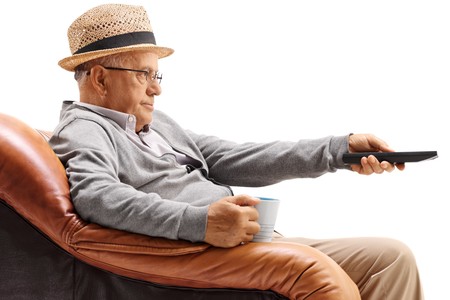 Bored elderly man sitting in an armchair and watching television isolated on white backgroundの写真素材