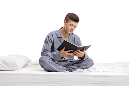 Teenager sitting on a bed and reading a book isolated on white backgroundの写真素材