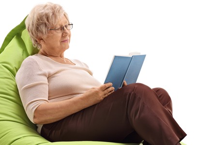 Mature woman sitting on a beanbag and reading a book isolated on white backgroundの写真素材