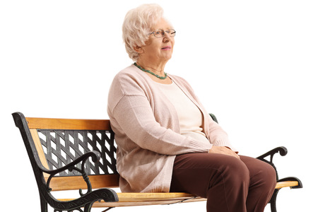 Pensive mature woman sitting on a bench isolated on white backgroundの写真素材
