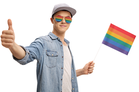 Teenager with a rainbow flag and glasses making a thumb up gesture isolated on white backgroundの写真素材
