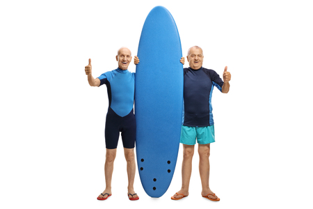 Full length portrait of two elderly surfers with a surfboard holding their thumbs up isolated on white backgroundの写真素材
