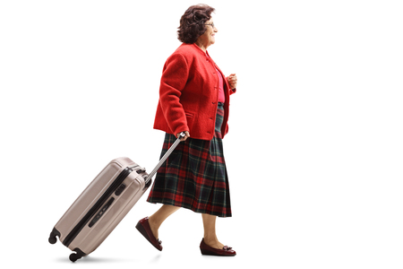 Full length profile shot of a senior lady walking and pulling a suitcase isolated on white backgroundの写真素材