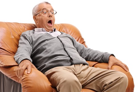 Terrified mature man sitting in an armchair isolated on white backgroundの写真素材