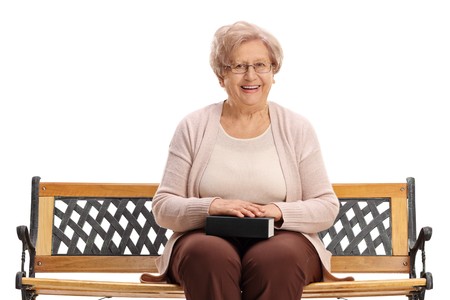 Mature woman with a book sitting on a bench isolated on white backgroundの写真素材