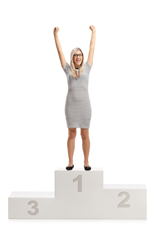 Full length portrait of an overjoyed young woman standing on a winners pedestal isolated on white backgroundの写真素材