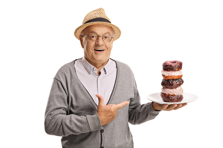 Smiling senior man holding a plate of donuts and pointing isolated on white backgroundの写真素材