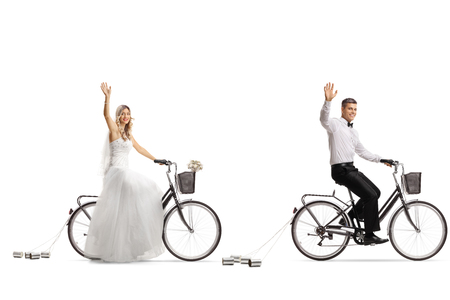 Bride and a groom riding bicycles and waving isolated on white backgroundの写真素材