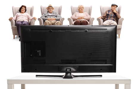 Two elderly women and two elderly men sitting in armchairs and watching televisionの写真素材