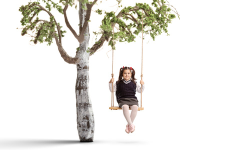 Little schoolgirl on a swing hanging from a tree branch isolated on whiteの写真素材