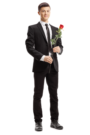 Full length portrait of a young elegant man holding a red rose and smiling at the camera isolated on white backgroundの写真素材