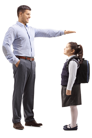 Full length shot of a young man in formal clotes gesturing with hand and showing the height of a little schoolgirl isolated on white backgroundの写真素材