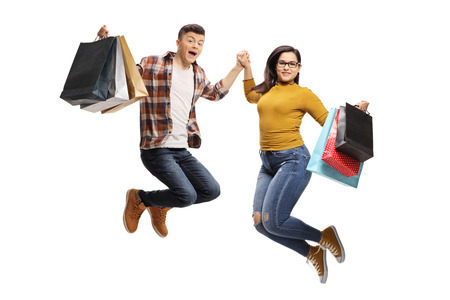 Full length portrait of energetic male and female teenagers jumping with shopping bags isolated on white backgroundの写真素材
