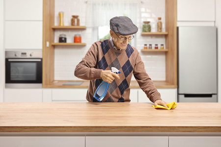 Elderly man cleaning a wooden counter in a kitchenの写真素材