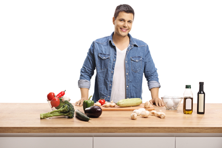 Smiling young guy cooking with healthy ingridients on a wooden counter isolated on white backgroundの写真素材