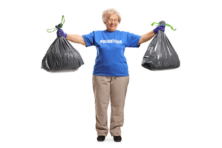 Full length portrait of an elderly woman volunteer posing with two waste bags isolated on white backgroundの写真素材