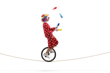 Full length profile shot of a clown juggling with clubs and riding a unicycle on a rope isolated on...