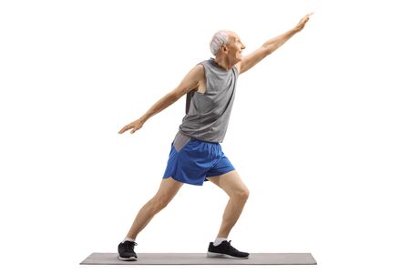 Full length shot of a senior man in sports clothes stretching on an exercise mat isolated on white backgroundの写真素材