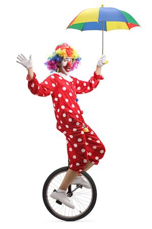 Full length shot of a clown riding a unicycle and holding an umbrella isolated on whiteの写真素材