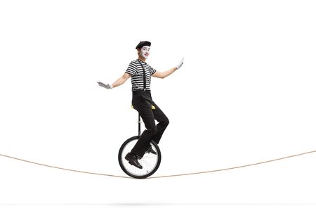 Full length profile shot of a mime riding a unicycle on a rope isolated on white backgroundの写真素材