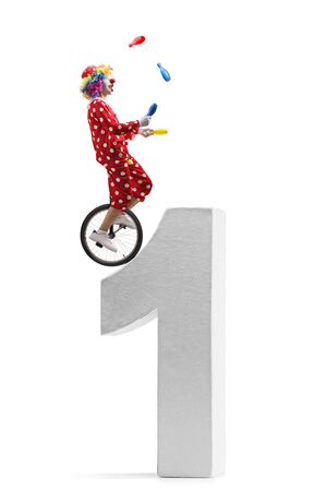 Full length profile shot of a clown juggling and riding a unicycle on a giant number one isolated on white backgroundの写真素材