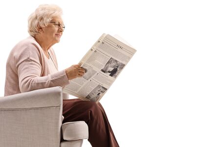 Profile shot of a senior woman sitting and reading a newspaper isolated on white backgroundの写真素材