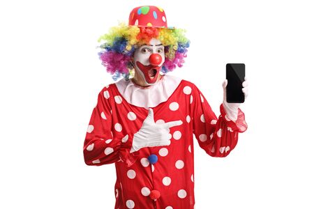 Cheerful clown holding a mobile phone and pointing at it isolated on whiteの写真素材