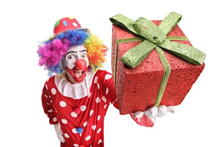 Excited funny clown holding a sparkly red gift box in front of the camera isolated on white backgroundの写真素材