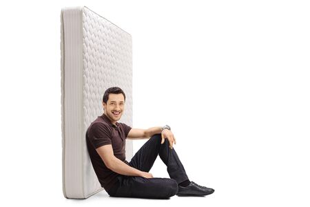 Young guy sitting on the floor and leaning against a bed mattress isolated on white backgroundの写真素材