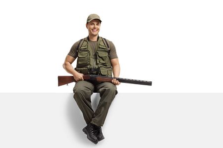 Young man hunter with a rifle sitting on a blank board isolated on white backgroundの写真素材
