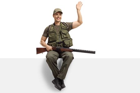 Hunter with a rifle sitting on a blank board and waving isolated on whiteの写真素材