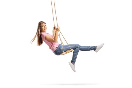 Full length shot of a young woman with long hair swinging on a wooden swing isolated on white backgroundの写真素材