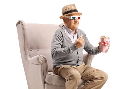Elderly man with 3d glasses and popcorn sitting in an armchair isolated on white backgroundの写真素材