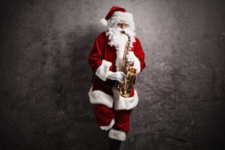 Santa Claus playing a saxophone and leaning on a rusty gray wall の写真素材