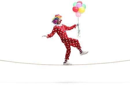 Full length profile shot of a clown walking on a rope and holding a bunch of balloons isolated on white backgroundの写真素材