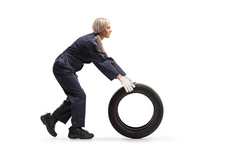 Full length profile shot of a female auto mechanic rolling a tire on the ground isolated on white backgroundの写真素材