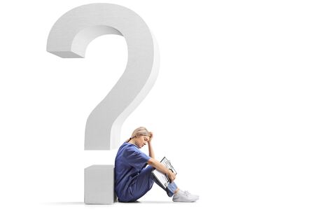 Tired female doctor sitting on the ground and leaning on a big question mark isolated on white backgroundの写真素材