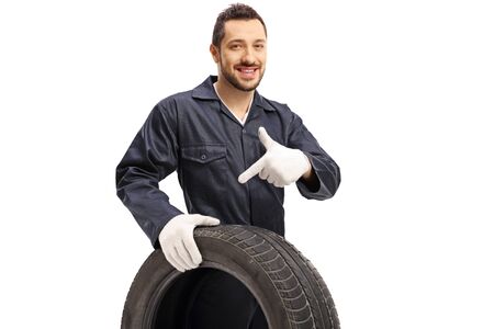 Auto mechanic holding a tire and pointing isolated on white backgroundの写真素材